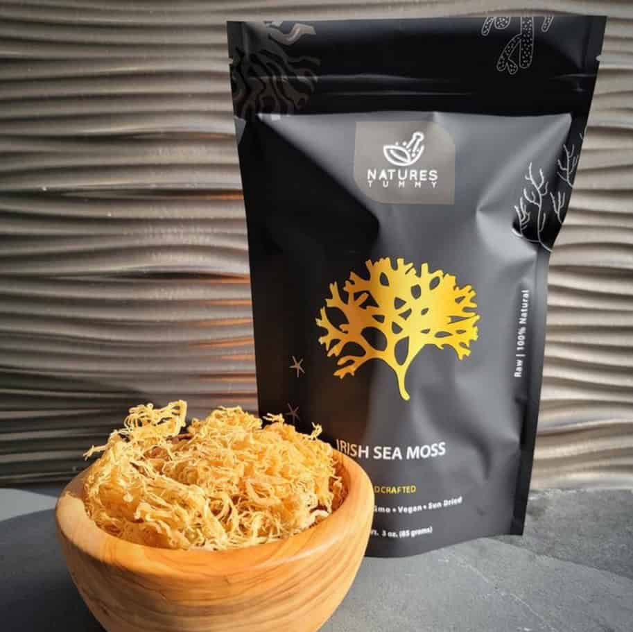 Irish sea moss supplement in resealable black packet with gold tree logo, placed next to fresh sea moss in a wooden bowl. Perfect for health-conscious consumers seeking natural, vegan, and sun-dried superfoods.